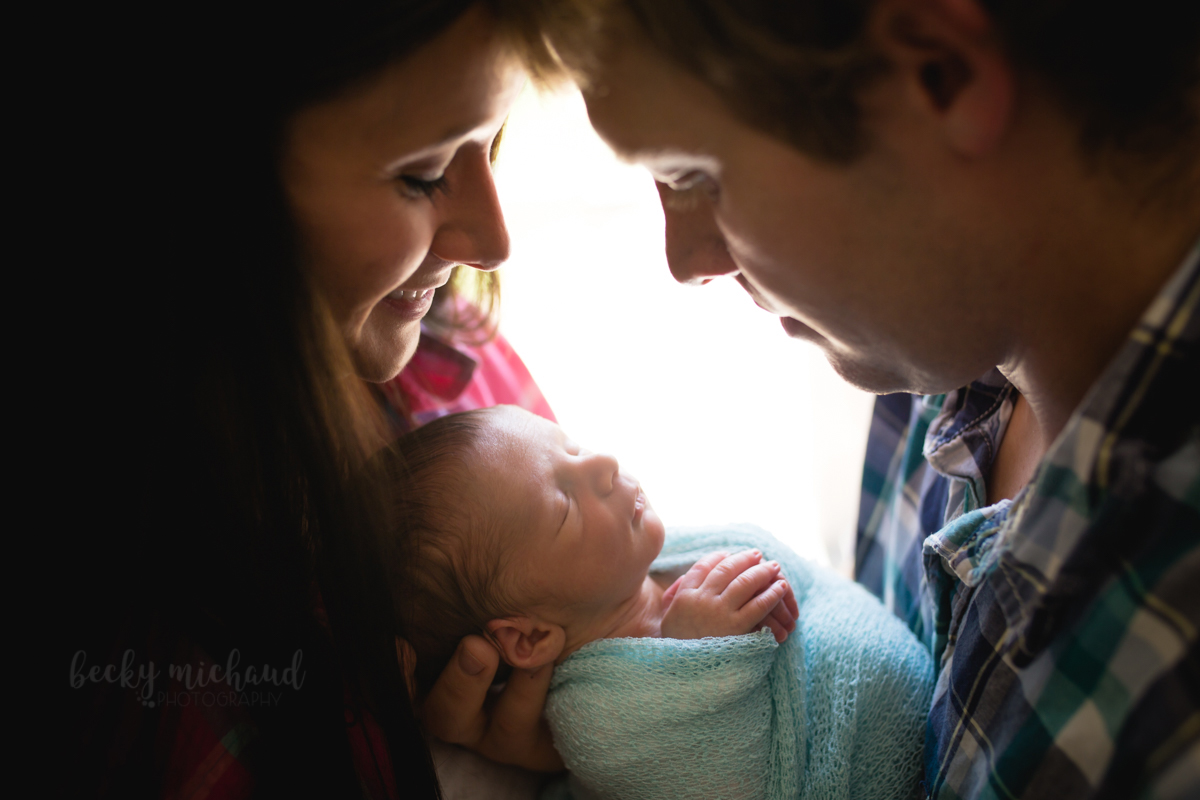 Backlit photo of a mom and dad smiling over their new baby boy during their Fort Collins newborn photography session