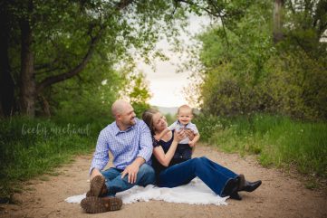 A family of three poses for their Fort Collins photographer by playing together in the woods