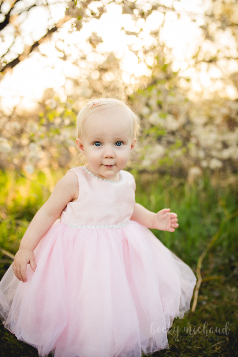 A baby girl wearing a pink dress plays by the flowers at Benson Sculpture Garden in Loveland, Colorado