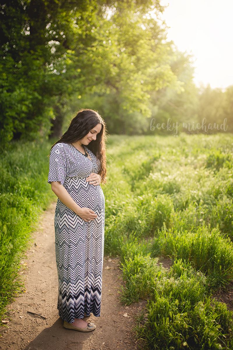 An expectant mom stands in beautiful sunlight and thinks about her baby coming soon