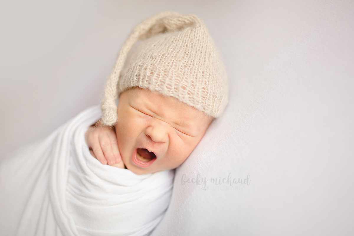 Simple minimalist newborn photo of a baby yawning while wearing a knit slouch hat