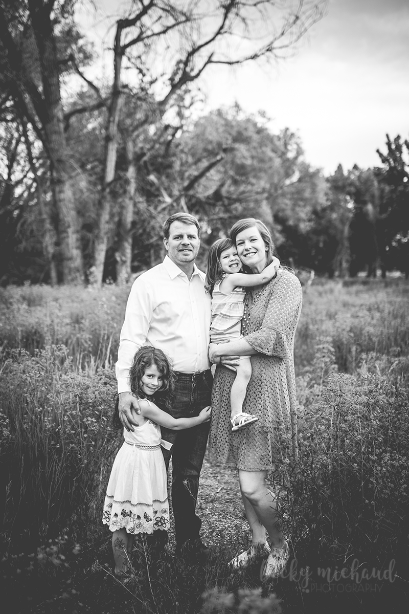 Black and white photo of a family of four hugging in a field in east Fort Collins