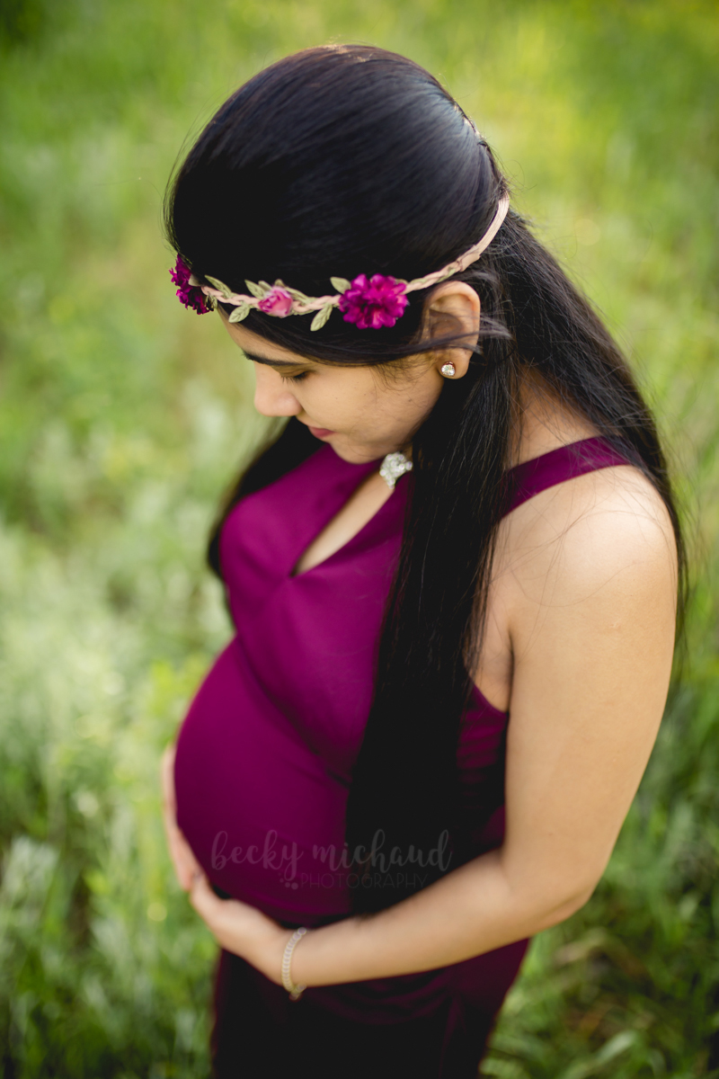 An expectant mom in a purple dress and crown looks at her belly in a photo taken by Becky Michaud, Fort Collins photographer