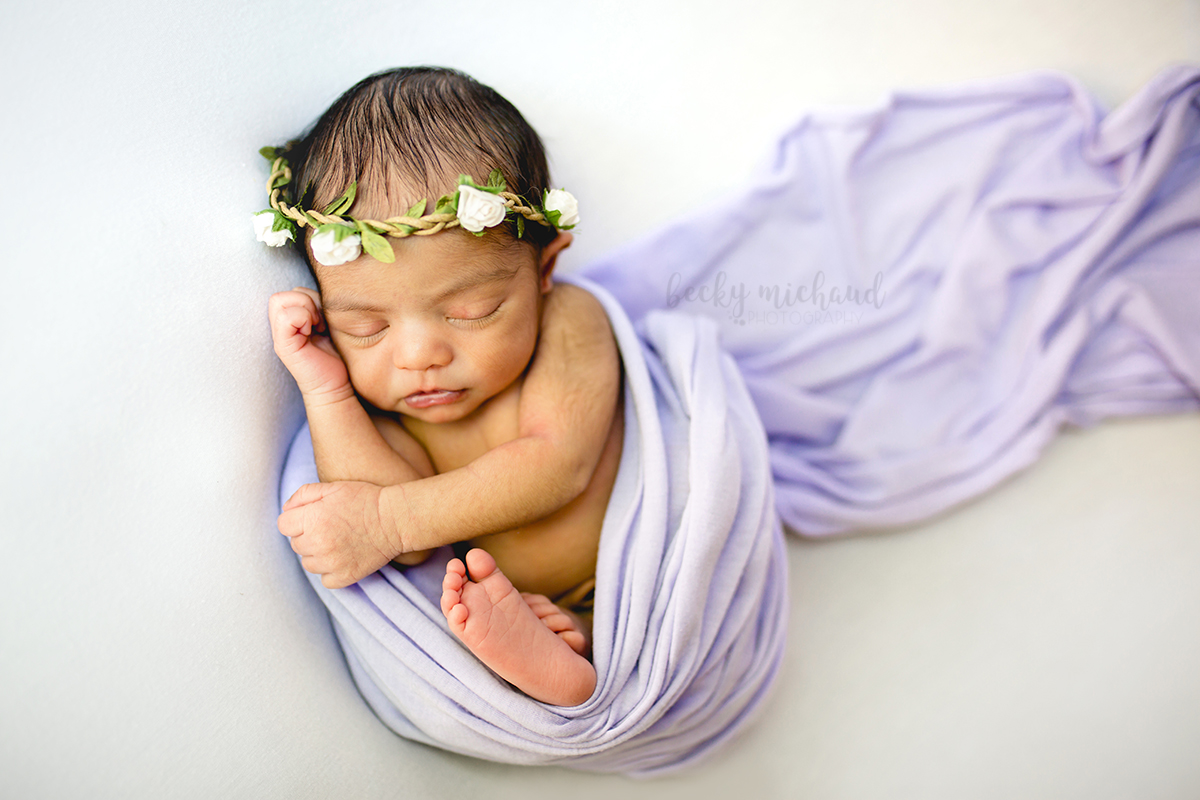 Sweet newborn girl wrapped in a purple wrap with a white flower crown