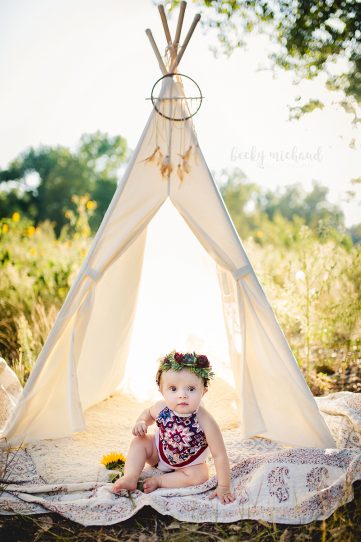 Boho style photo shoot in Fort Collins Colorado of a baby girl in an aztec print romper sitting by a cream colored teepee
