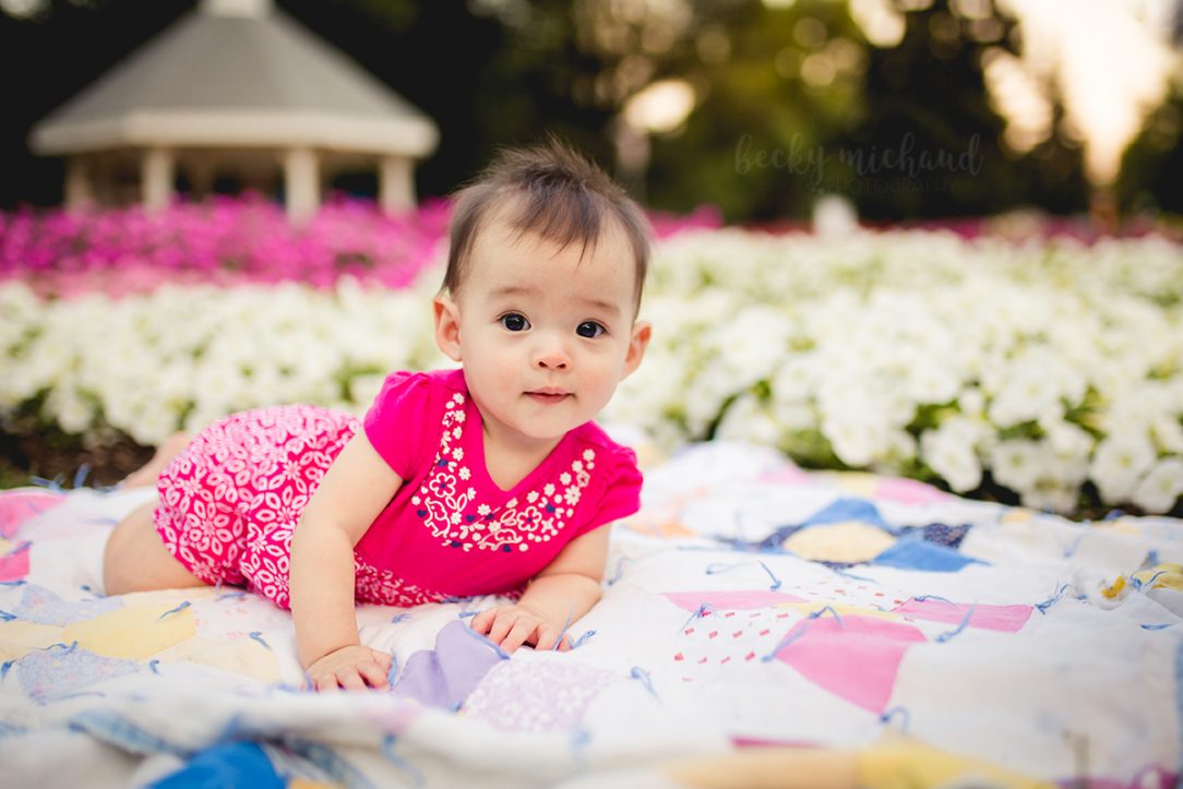 Baby girl plays on a vintage quilt in a flower garden in Fort Collins, CO
