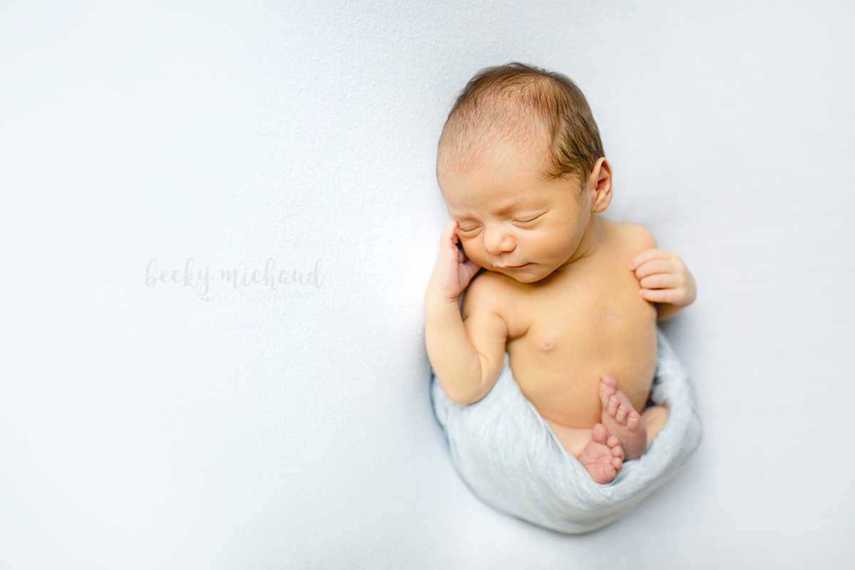 A baby boy poses on a white blanket for his in-home newborn photo session in Fort Collins, COlorado