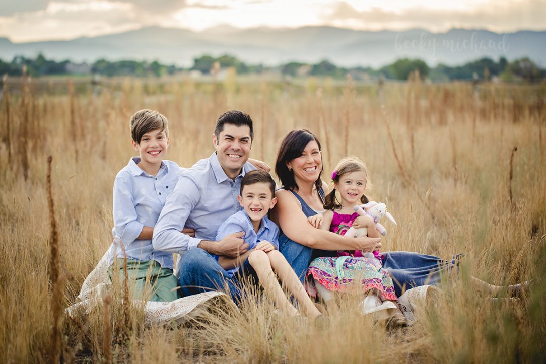 A family poses in a field with the Colorado mountains in the background during their outdoor family photo session