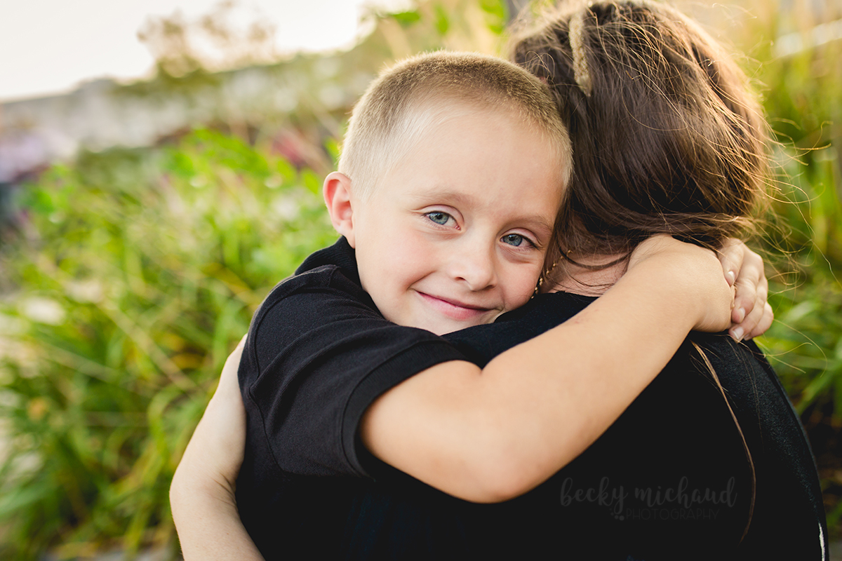 A boy hugs his mom and smiles while taking family photos in Old Town