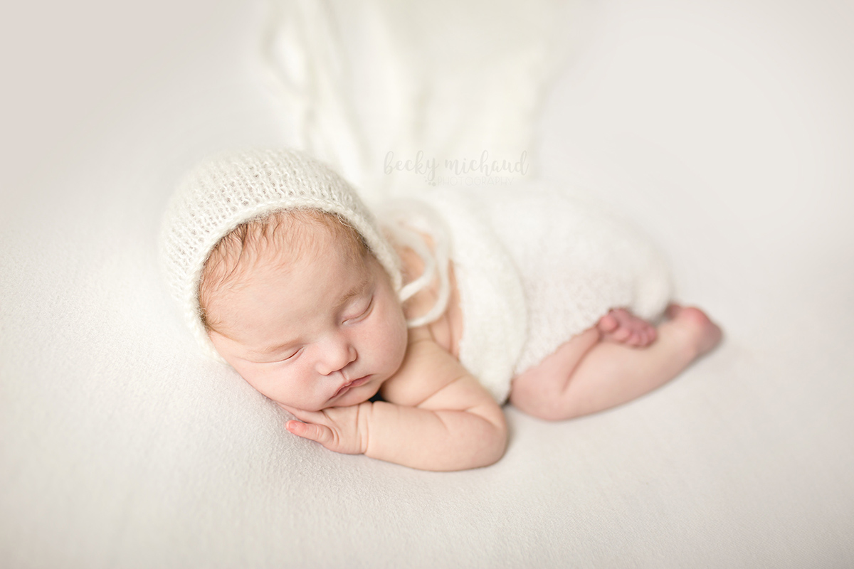 Simple and classic newborn photo of a baby in a white bonnet taken by Becky Michaud, newborn photographer serving Northern Colorado