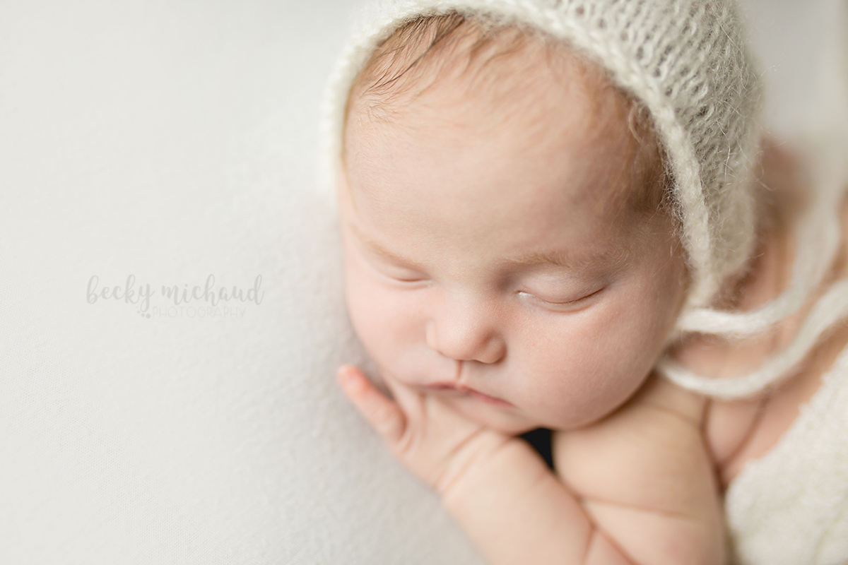 Newborn photo of a baby in a white bonnet in her Fort Collins home