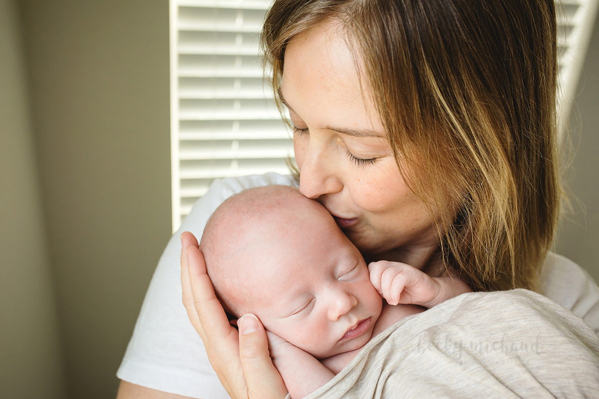 A mom kisses her baby during their newborn photo shoot in their home