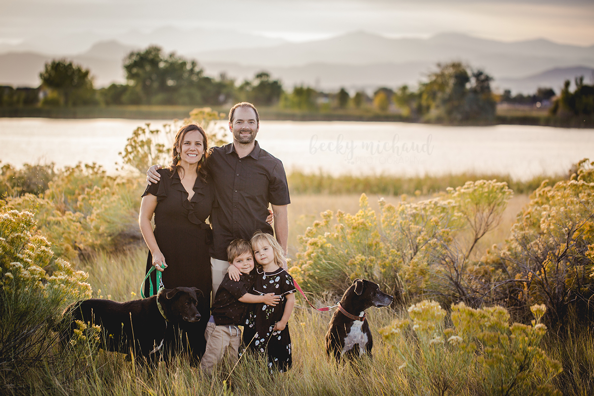 A family and their two dogs pose by a lake in Loveland Colorado with the mountains in the distance