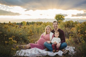 A family of three sits on a blanket with the sun setting behind them during their maternity photo shoot in Fort Collins, Colorado