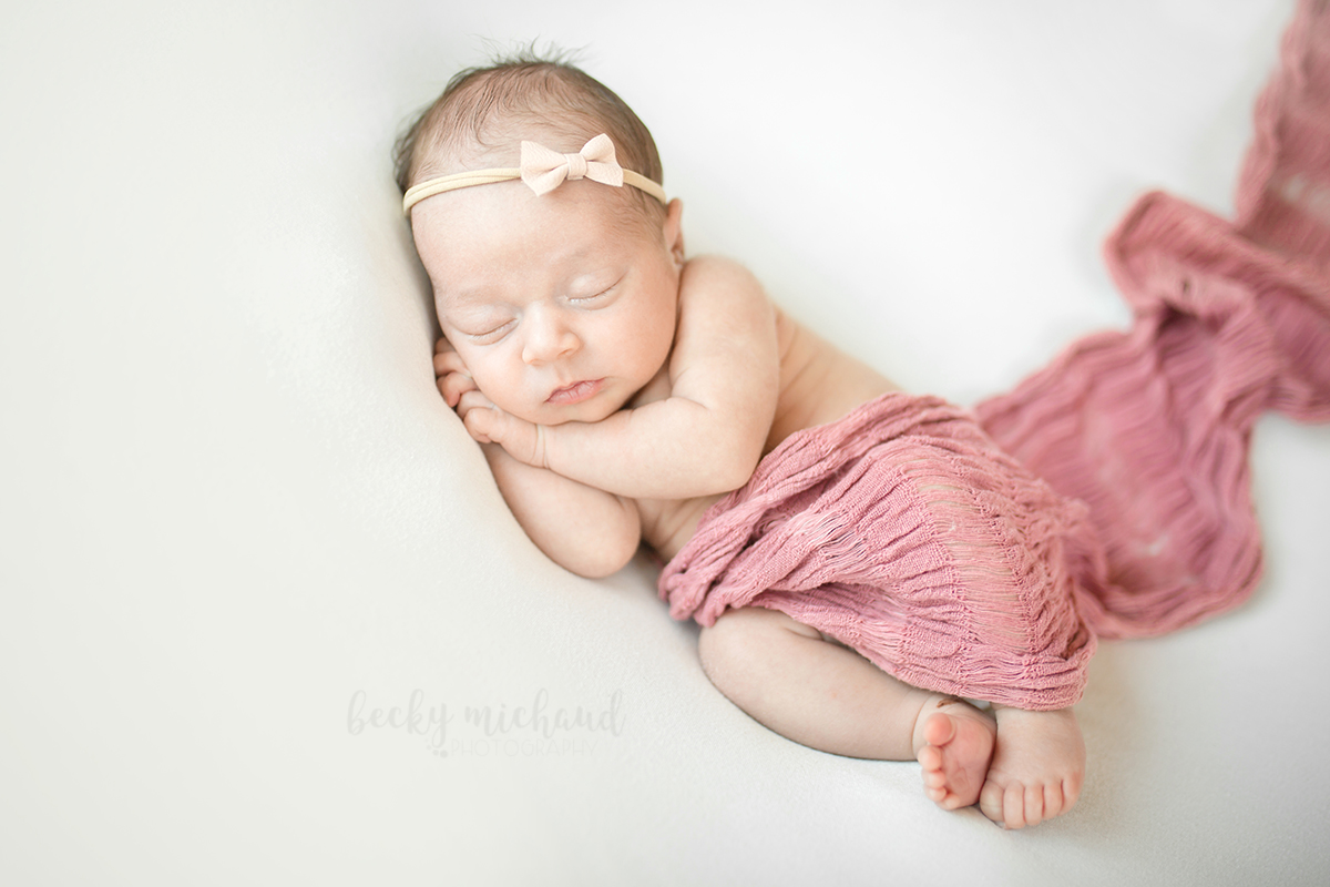 Baby girl on a white blanket with a pink bow and wrap