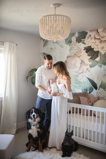New parents admire their baby girl in her beautiful nursery with their dogs by their side in a photo taken by Becky Michaud, Fort Collins newborn photographer