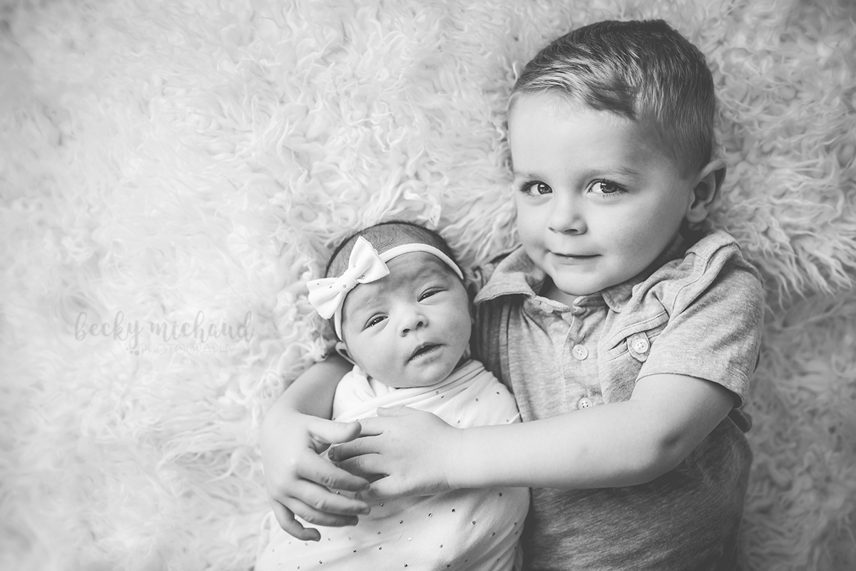 Black and white photo of two siblings posing together on a blanket for newborn photographer Becky Michaud in their Fort Collins home