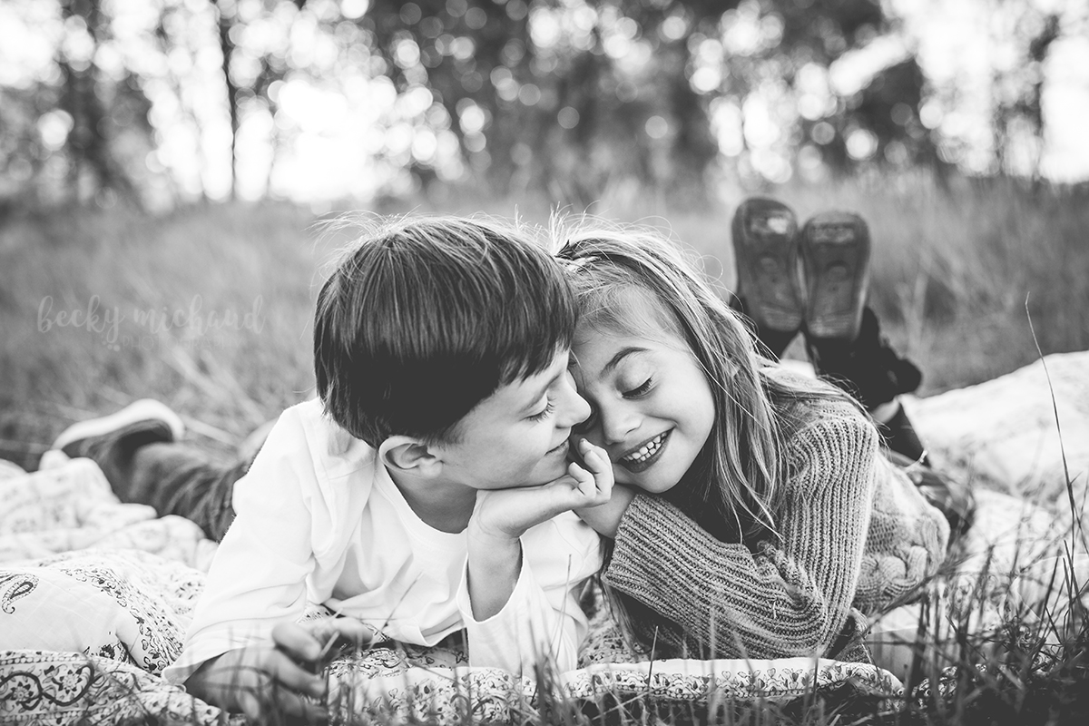 black and white photo of a pair of siblings cuddling together on a blanket during an outdoor family photo session in Northern Colorado