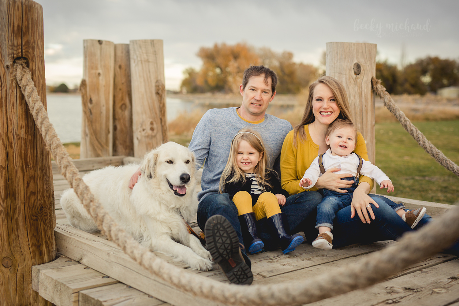 A family of four sits on a dock in Windsor Colorado with Windsor Lake behind them
