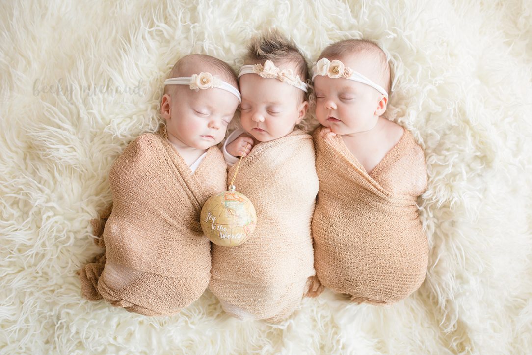 newborn triplet sisters on a neutral background with a Christmas ornament