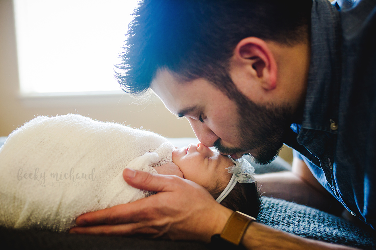 A new dad kisses his baby daughter on the forehead during her newborn photo session