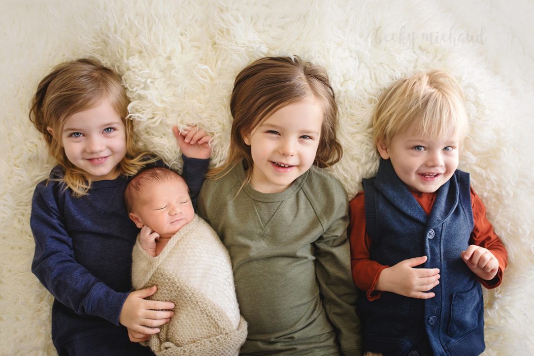 A newborn baby cuddles with his three older siblings during their photo shoot in the comfort of their home