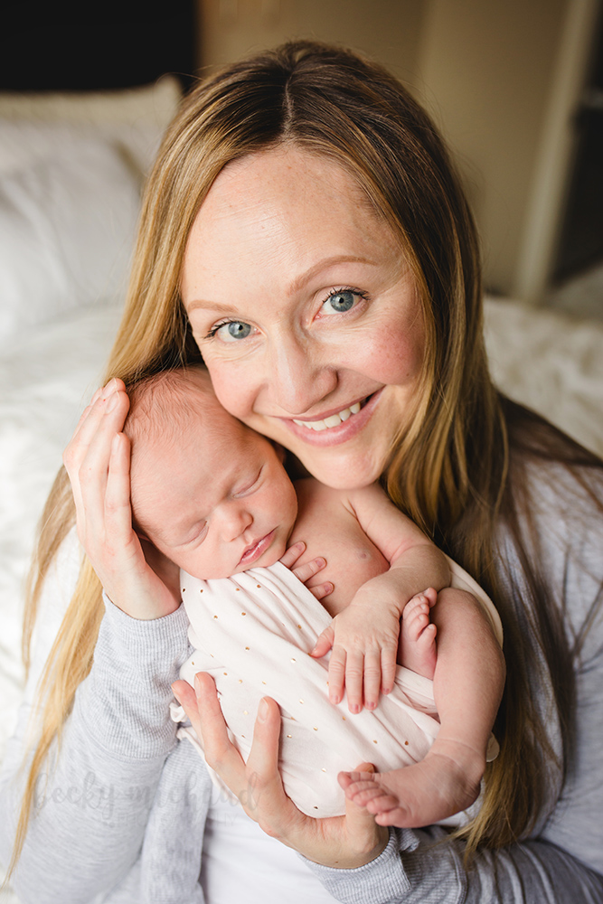 A mom cradles her newborn baby daughter as she poses for the camera during their in home newborn photo session in Colorado