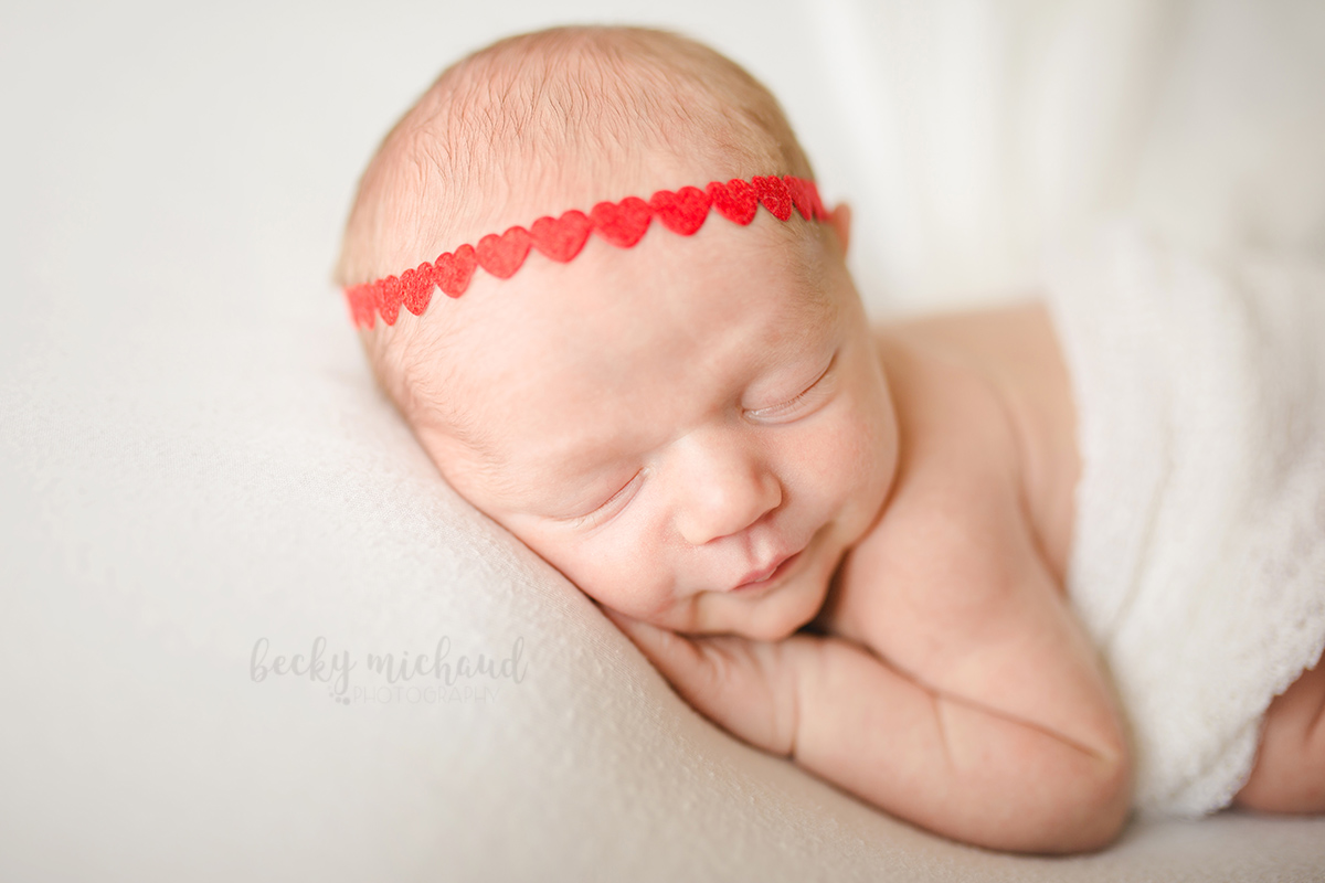 Close up photo of a baby girl wearing a red  heart headband 