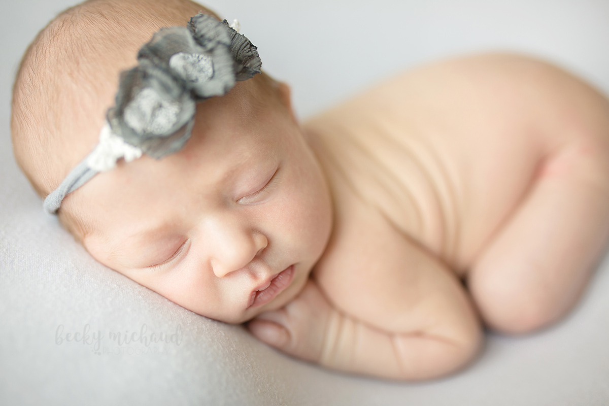 Sweet newborn baby girl with a grey headband in a posed newborn photo taken in her home in Loveland, Colorado