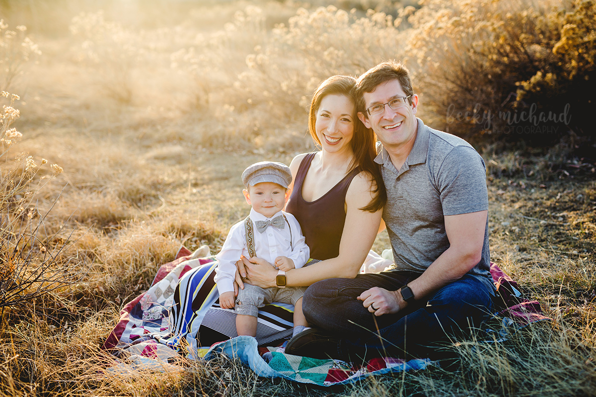 A family of three sits on a blanket in golden light in Loveland, Colorado