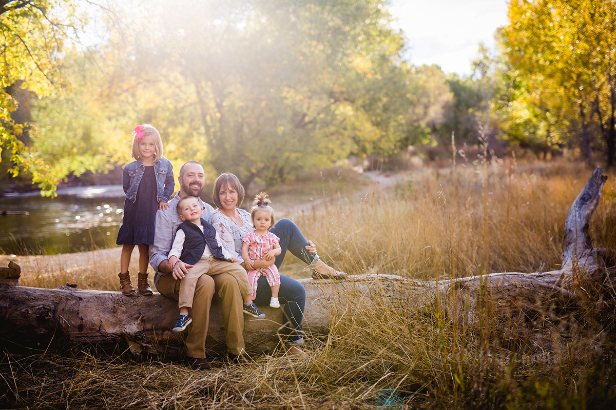 Parents and their three kids sit on a log as they pose for their family photos in Fort Collins