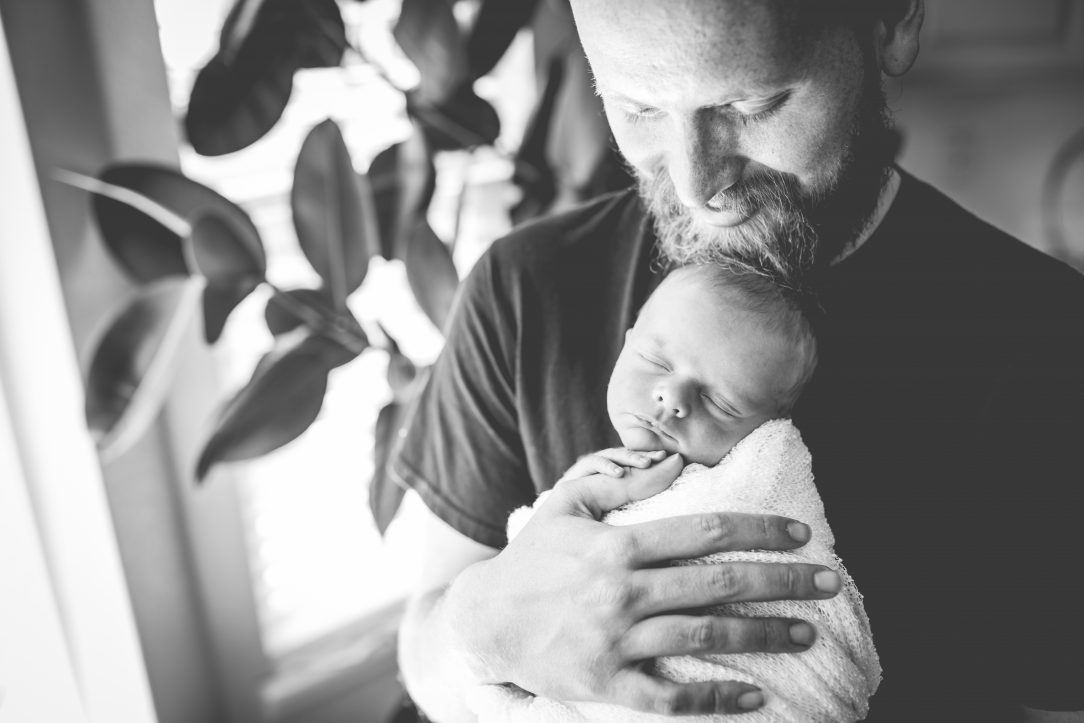 A proud dad looks down on his newborn boy in a black and white photo taken near a window in their Fort Collins home
