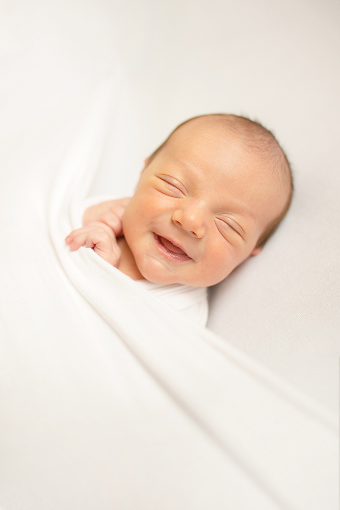 A newborn baby boy smiles in a simple newborn photo taken in his Fort Collins home