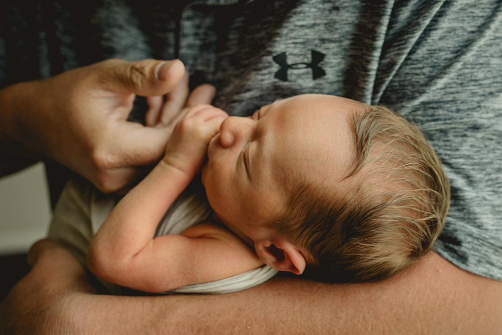 A baby holds on to his dad's hand in their Wellington, Colorado home