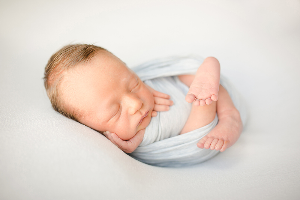 Photo of a baby boy all curled up for his newborn photography session in his home in Wellington, Colorado