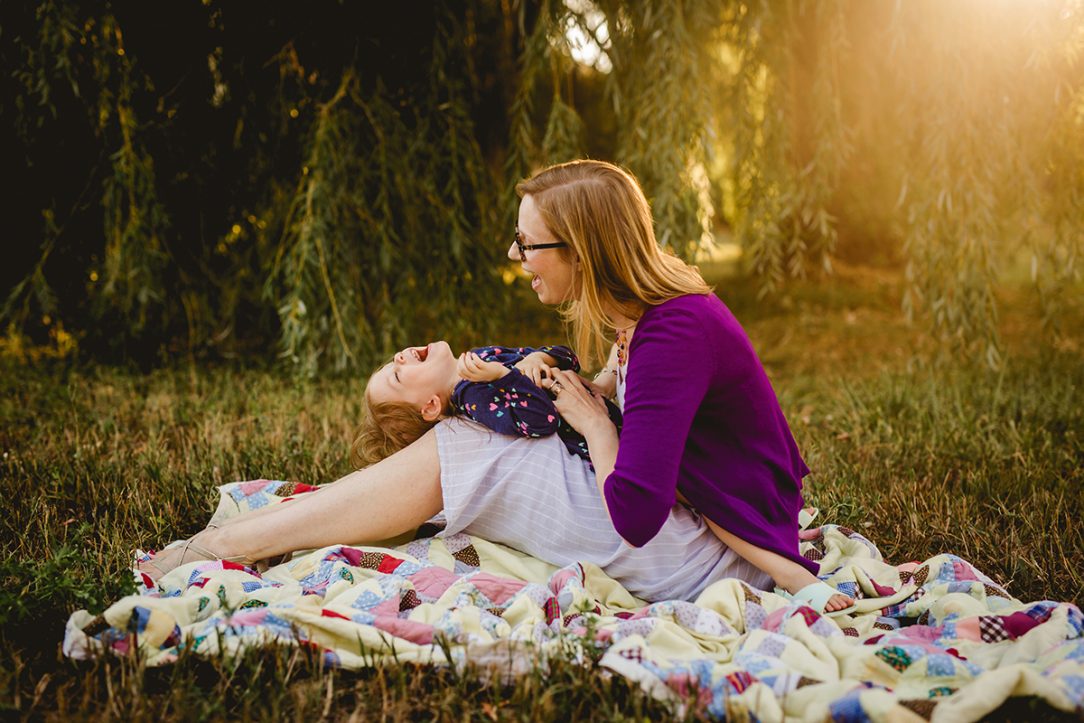 Mom tickles her daughter under a willow tree as they pose for their family photos in Fort Collins, Colorado