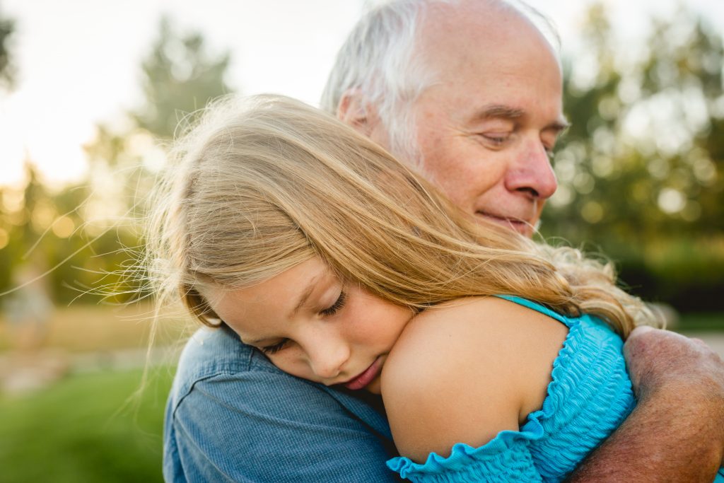 A girl snuggles into her grandpa's shoulder during their family photography session at Chapungu Sculpture Park