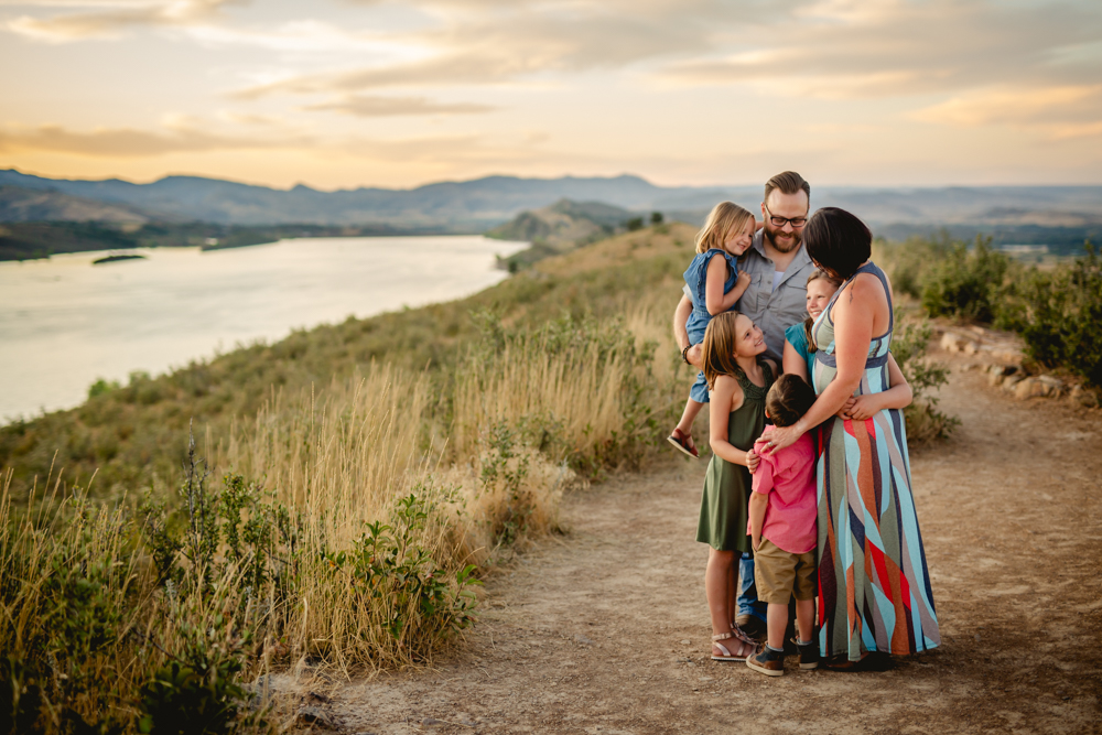 A family of six stands on a hill at Horsetooth Reservoir as the sunsets over the foothills