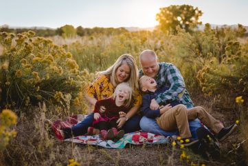 A family laughs together while they sit in a field, posing for a photo by Becky Michaud, Colorado photographer