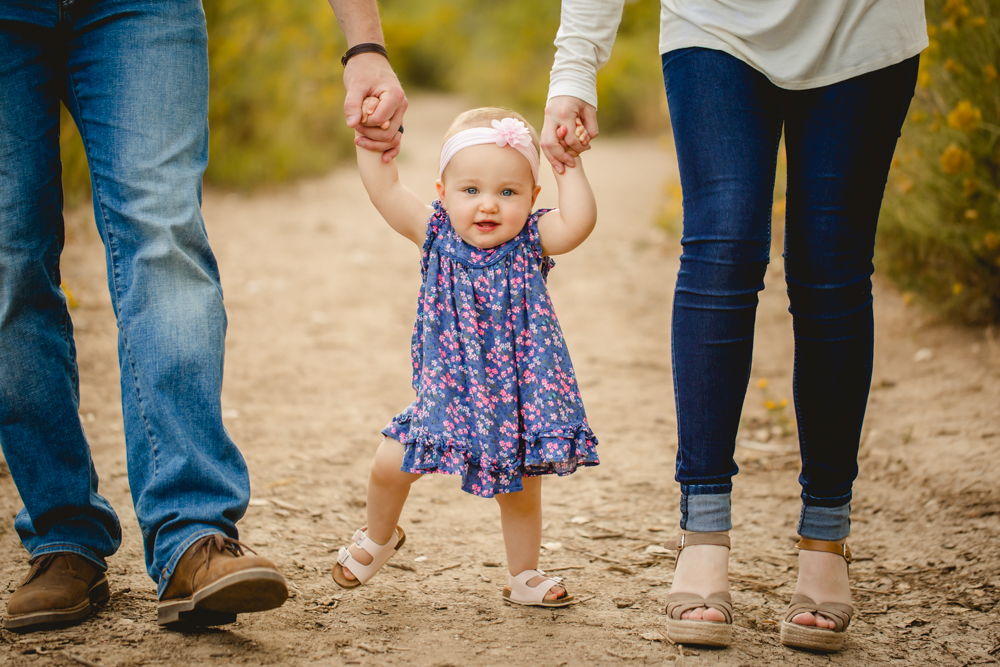 Baby girl walks between her parents during their family portrait session in Fort Collins, Colorado on a fall day