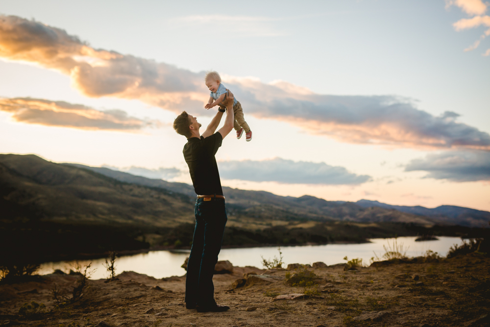 Dad holds his baby high as the sun sets over Horsetooth Reservoir during their Fort Collins family photo session