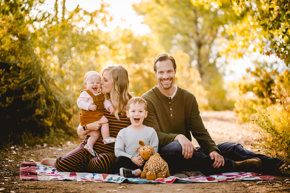 A family of four sits on a blanket in the golden fall leaves during their Fort Collins family photo session