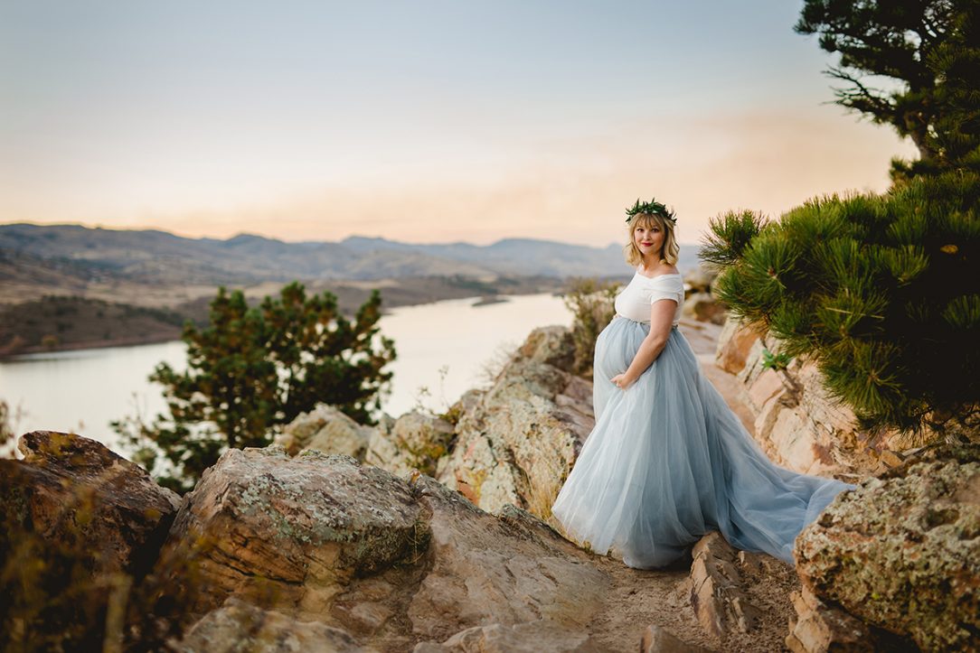 An expectant mother stands above Horsetooth Reservoir as she poses for her maternity photography session