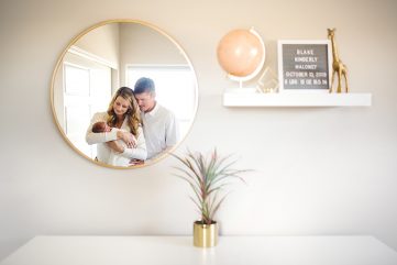 a new family of three is reflected in a mirror in the baby's Loveland, Colorado nursery