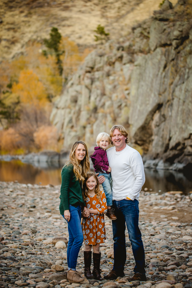A family of four stands by the Poudre River at Picnic Rock as they pose for their family photo session