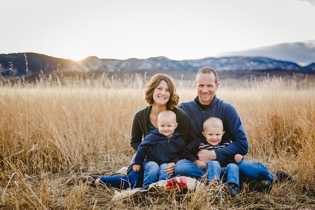 A family of four poses in a field with the snowy mountains in the background during their family photography session in Fort Collins