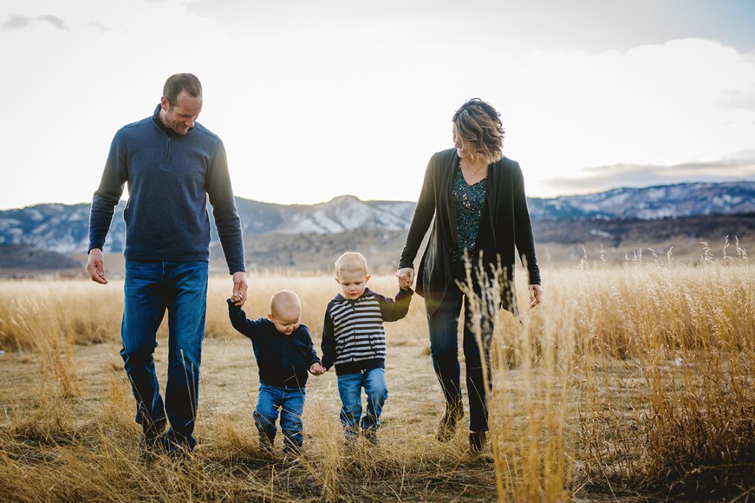A family of four walks in a field with the Colorado foothills behind them