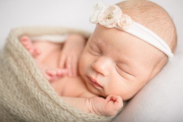 Sweet baby girl wearing a floral headband and a neutral wrap in a newborn photo taken by Becky Michaud, Fort Collins photographer