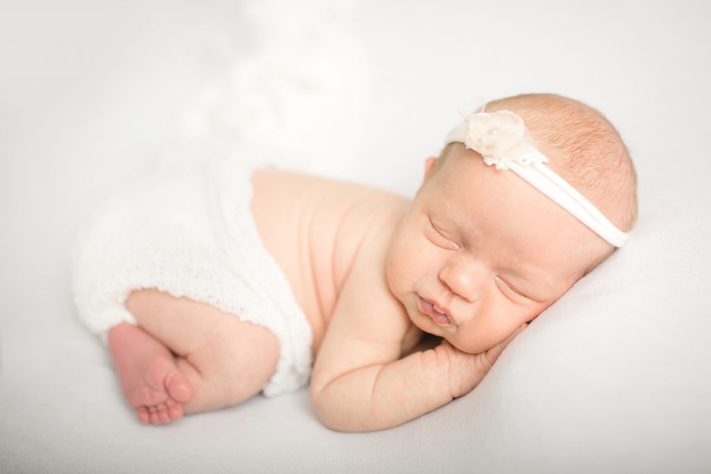Photo of baby girl in white, taken during her in home newborn photography session in Johnstown, Colorado