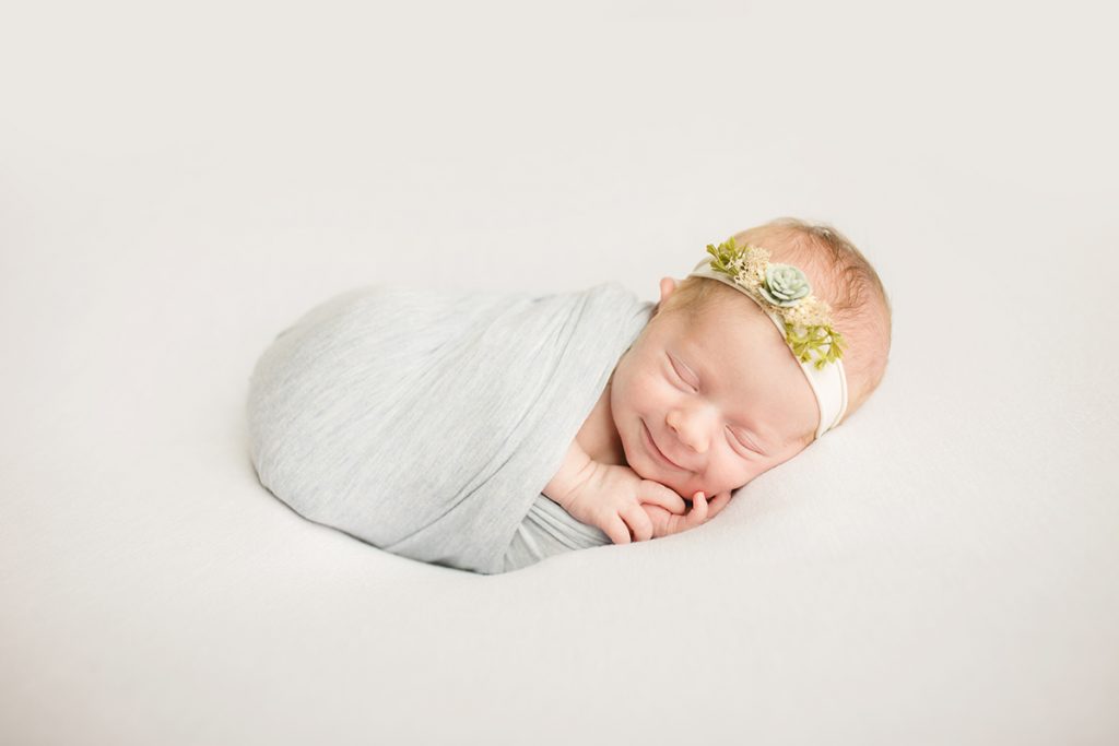 Smiling newborn lying on a white blanket wearing a succulent headband